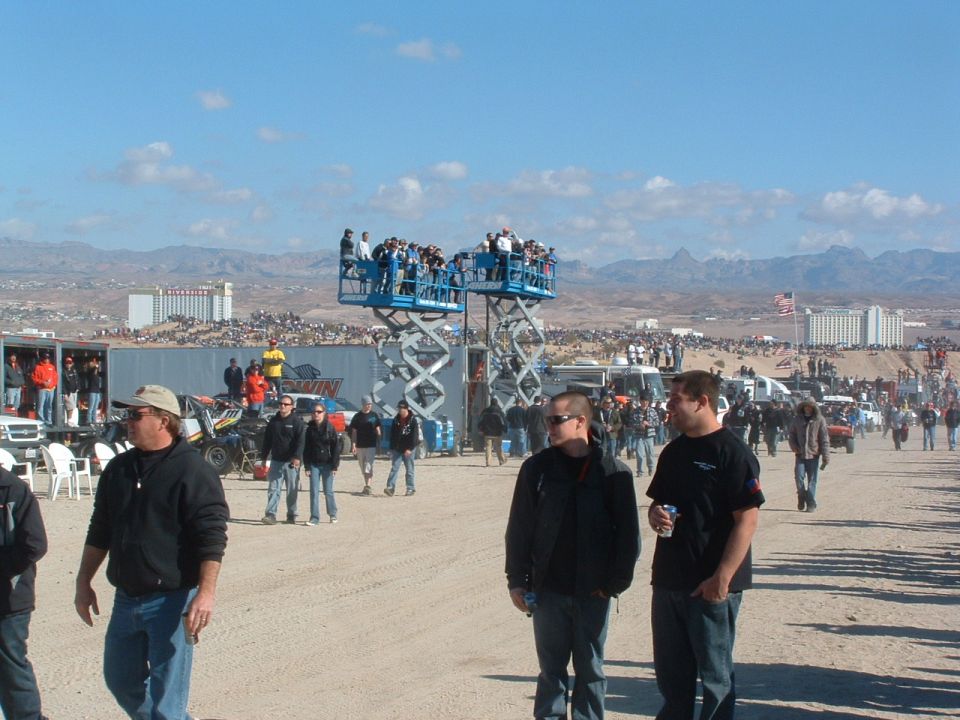 Outdoor event scene with people, scissor lifts, and distant buildings under a blue sky