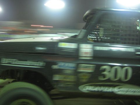 Black off-road race truck number 300 in motion at night with Deaver decal on door