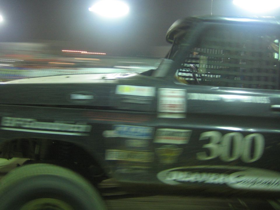 Black off-road race truck number 300 in motion at night with Deaver decal on door