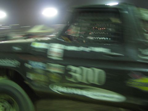 Heavily motion-blurred black race truck number 300 at night with sponsor stickers