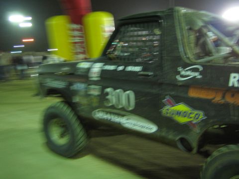 Black race truck number 300 with Sunoco decal passing yellow barrels at night