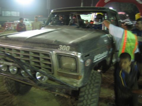 Front of vintage Ford race truck number 300 with crew and worker in safety vest at night