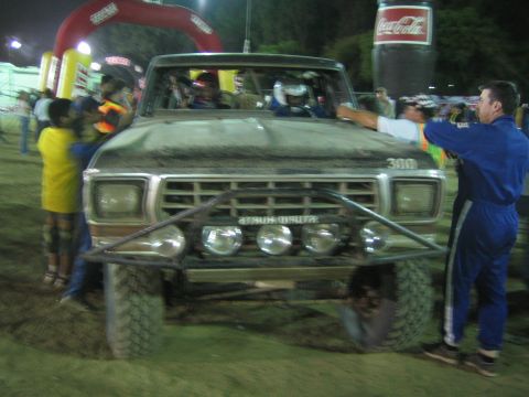 Front of muddy Ford race truck 300 with light bar under Coca-Cola arch at night