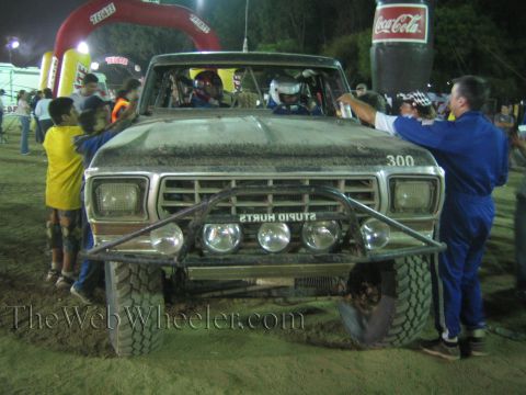 Front of Ford race truck 300 with STUPID HURTS bumper text and crew at night