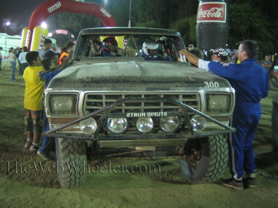 Front of Ford race truck 300 with STUPID HURTS bumper text and crew at night