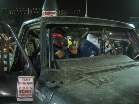 Race truck cab with helmeted driver and 2005 SCORE Class Champion placard on window