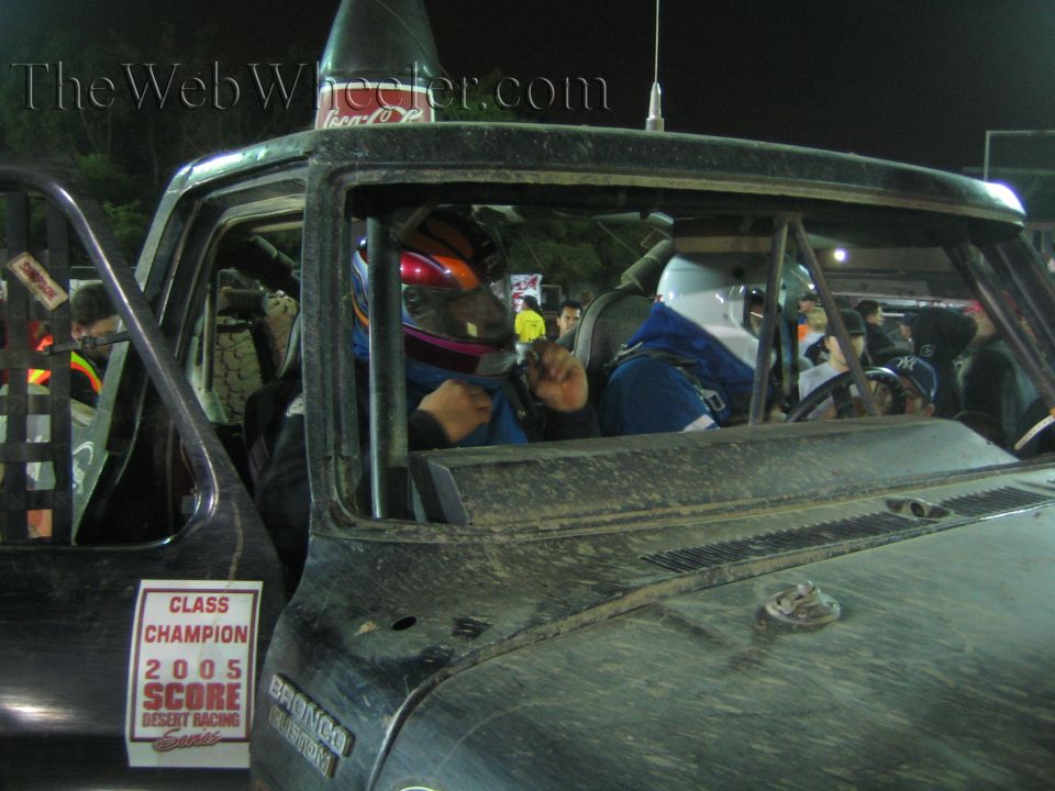 Race truck cab with helmeted driver and 2005 SCORE Class Champion placard on window
