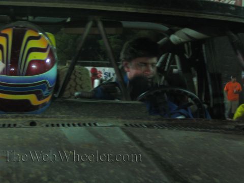Driver in glasses at the wheel of a race truck beside a colorful helmet at night