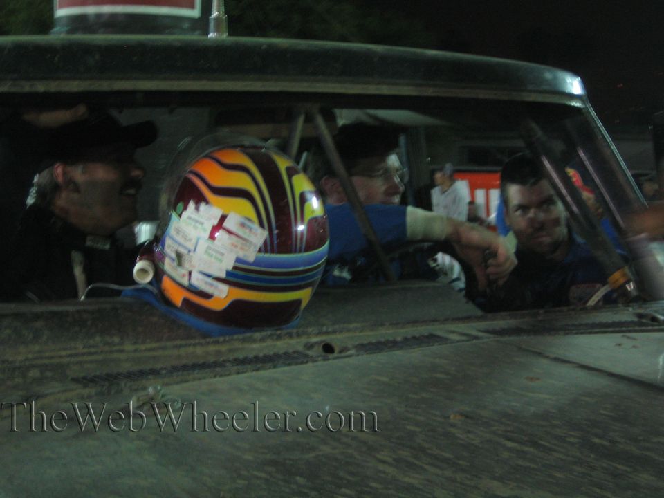 Colorful sticker-covered racing helmet on a dusty race truck dash at night
