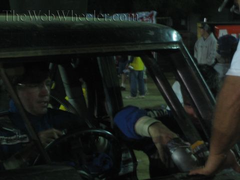 Bespectacled man in blue at the wheel of a race truck receiving a handed-over item at night