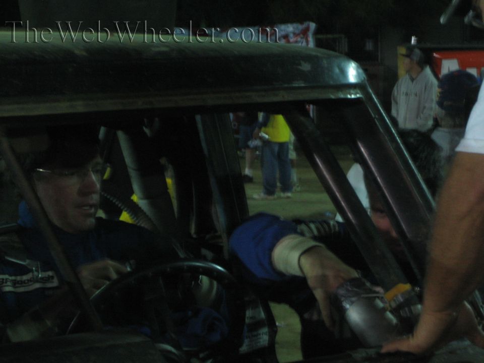 Bespectacled man in blue at the wheel of a race truck receiving a handed-over item at night