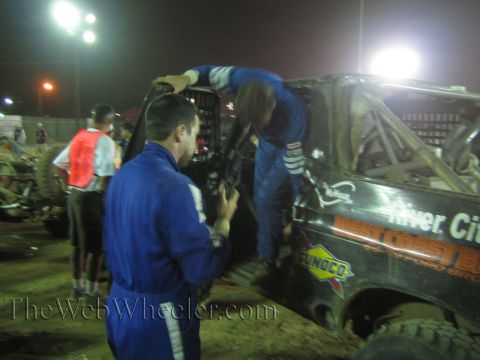 Crew in blue suits climbing into a black race truck with West Coast and Sunoco decals at night