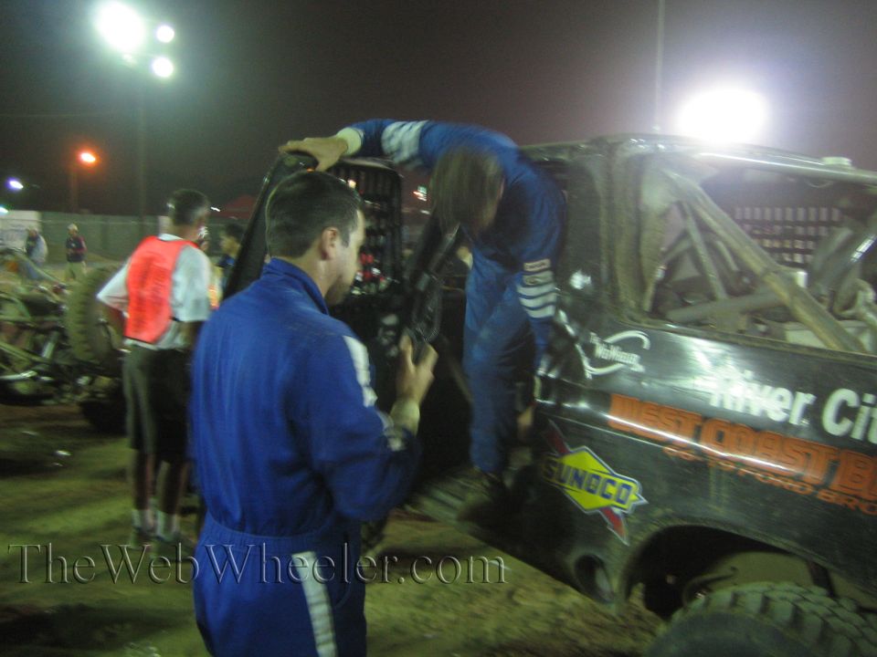 Crew in blue suits climbing into a black race truck with West Coast and Sunoco decals at night