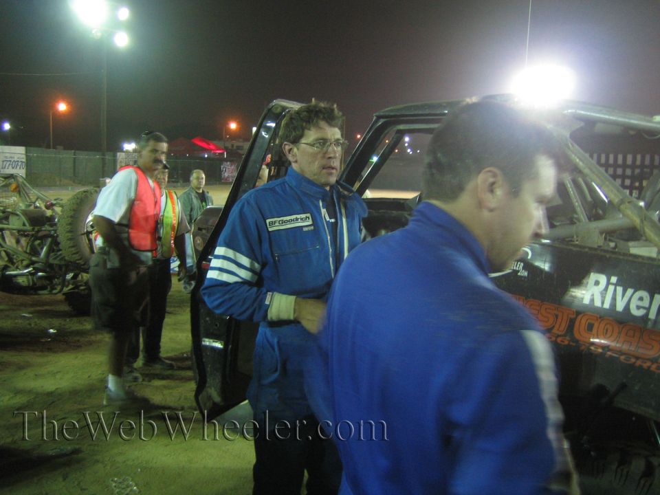 Men in blue BFGoodrich race suits talking by black race truck at night
