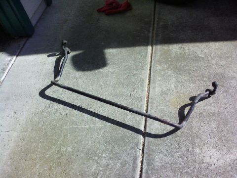 1995 Ford Bronco - A sway bar lies on a concrete surface, casting a long shadow.