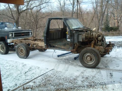 1989 Ford F-250 - A truck cab and chassis sits on the ground, with another truck behind it in a snowy outdoor setting.