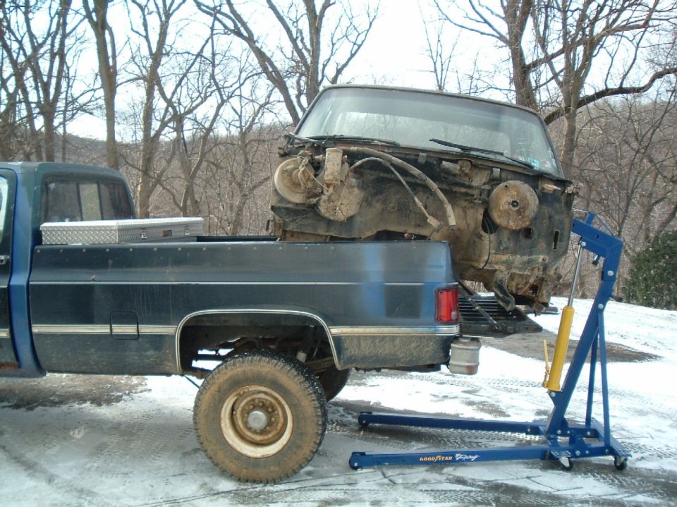 Engine hoist lifting disassembled vehicle front end from truck bed