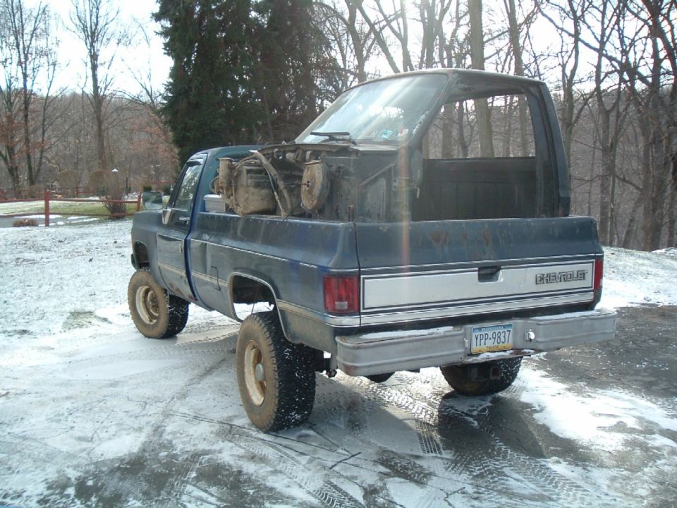 Blue Chevrolet pickup truck, lifted, with engine parts in the bed, parked on a snowy driveway