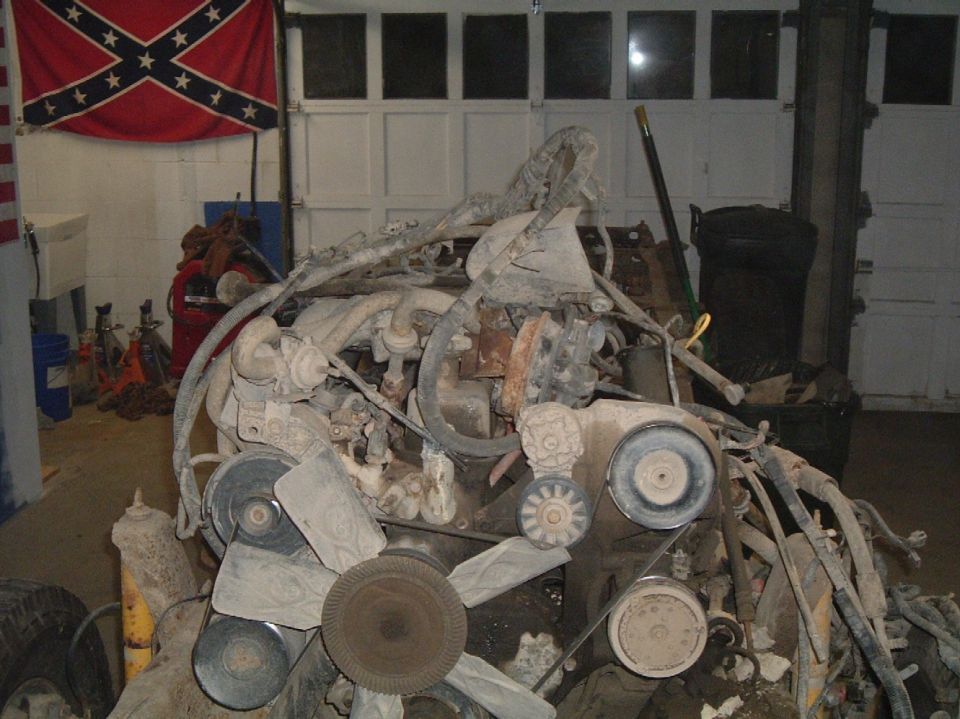 Engine assembly with fan, belts, and hoses. Garage in background with a flag