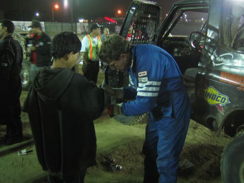 Man in blue racing suit shakes a youth's hand by a Sunoco race truck at night