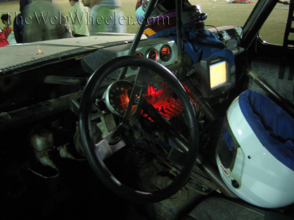Interior of a stripped off-road race vehicle with steering wheel and red-lit gauges