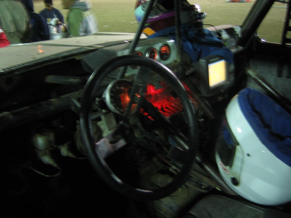 Dim race-vehicle cockpit with steering wheel, gauges and a white helmet on the seat