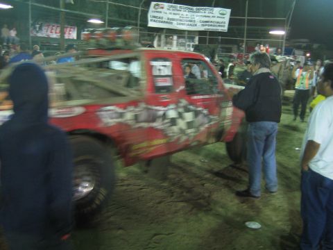 Red off-road race truck with sticker-covered doors in a lit dirt arena at night