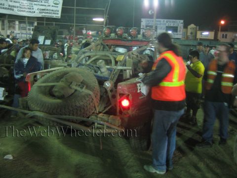 Crew in safety vests inspect the rear of a race truck with spare tires at night