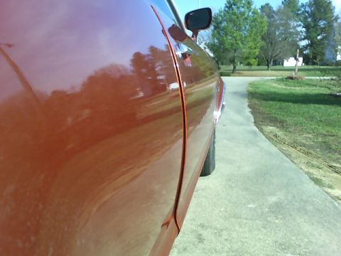 1979 Ford Ranchero - Side profile of a red vehicle, with a clear reflection of trees and sky on its polished surface.