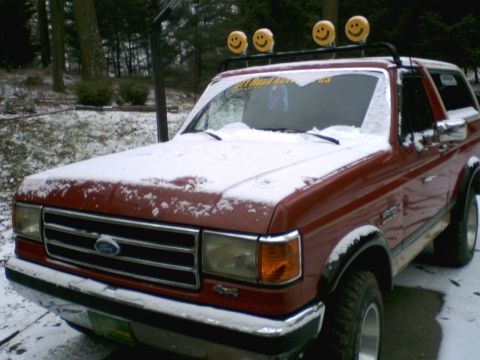 1989 Ford Bronco - A red Ford Bronco sits in the snow, equipped with a roof rack and four smiley face lights.