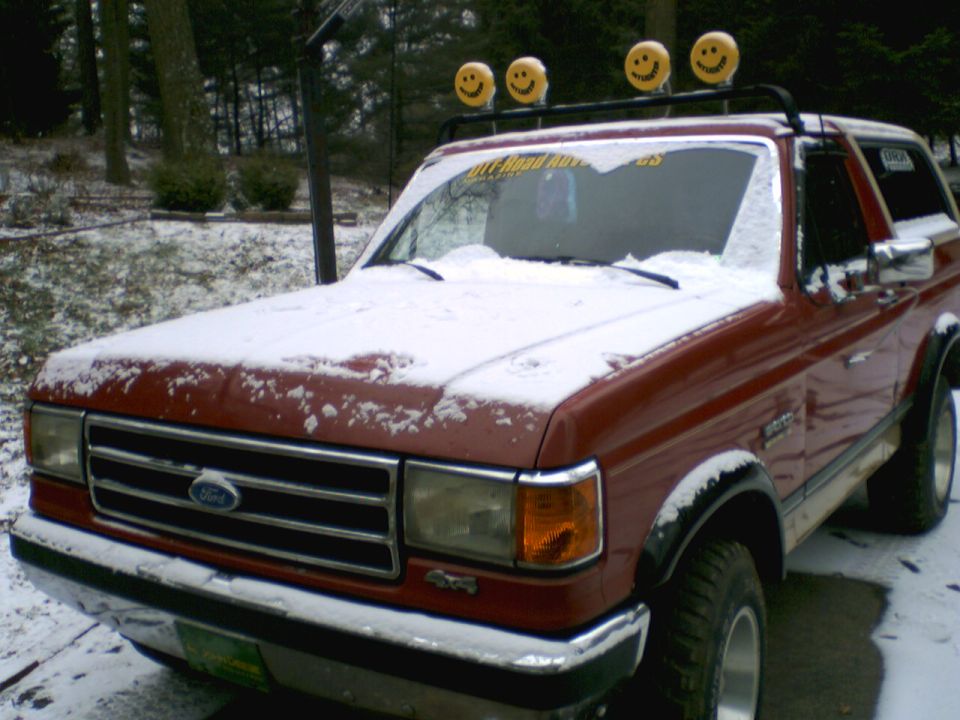 Red Ford Bronco with snow on hood and roof, four smiley face lights on roof rack
