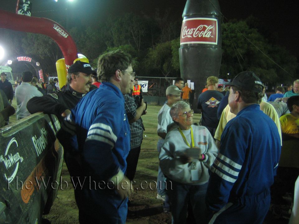 Crowd in racing suits stands near a giant inflatable Coca-Cola bottle at night