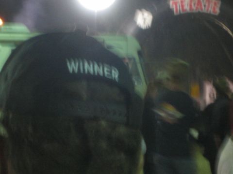 Back of a camouflage cap reading WINNER in a crowd under a Tecate sign at night