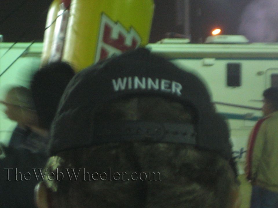 Back of a black WINNER cap with a parked RV in the background at night