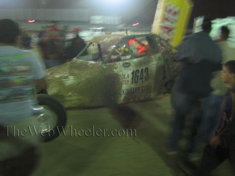 Mud-caked race buggy numbered 1643 moves past a crowd in a lit arena at night