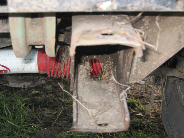 Close-up of dirty vehicle frame with red suspension components and grass