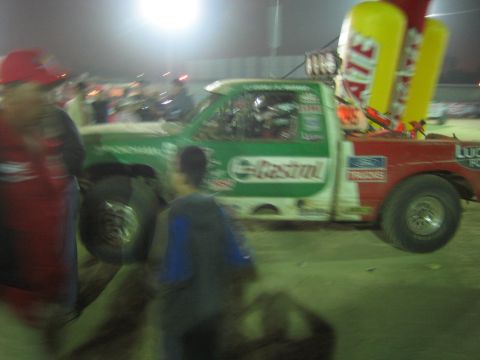 Green Castrol off-road race truck passing spectators at night, motion blurred