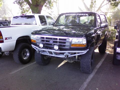 1995 Ford Bronco - Three-quarter front view of a lifted black full-size Ford Bronco in a parking lot, fitted with a white tubular front bumper with dual round…