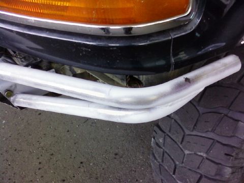1995 Ford Bronco - Close-up of a vehicle's front bumper with custom pipes and a tire visible.