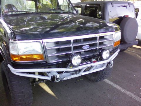 1995 Ford Bronco - Front view of a lifted black Ford truck with chrome grille, winch, tube bumper and round driving lights.