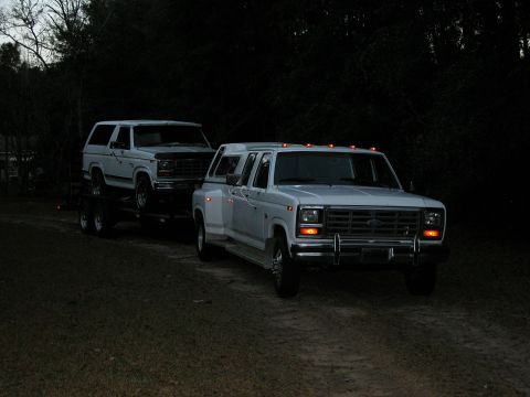 1986 Ford F-350 - A white dually truck tows a white SUV at dusk.