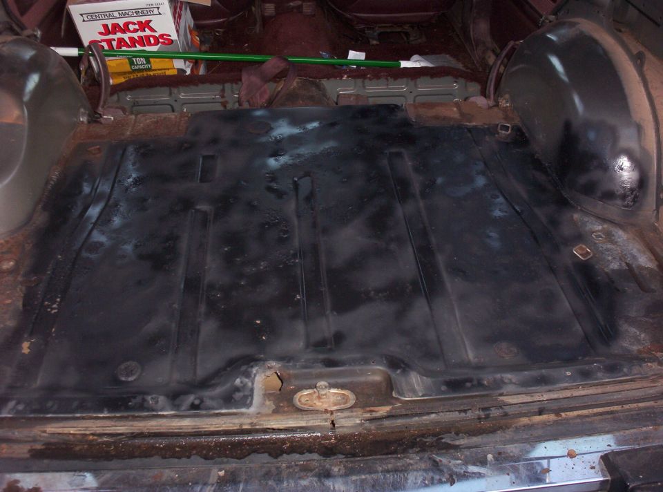 Cargo area floor with black matting, showing rust on edges. Box of jack stands visible