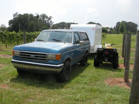 1990 Ford Bronco - A blue Ford Bronco from the late 1980s is seen towing a trailer with an ATV nearby.