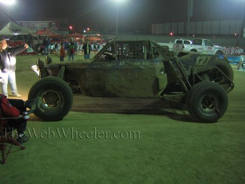 Tube-frame off-road buggy number 127 parked on dirt at night under lights