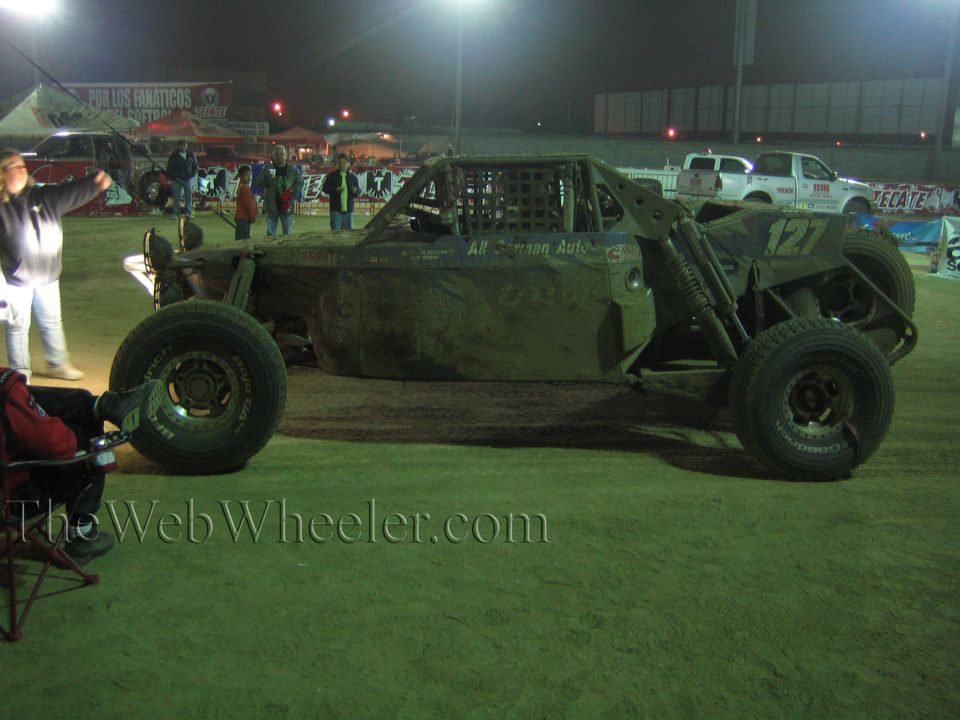Tube-frame off-road buggy number 127 parked on dirt at night under lights