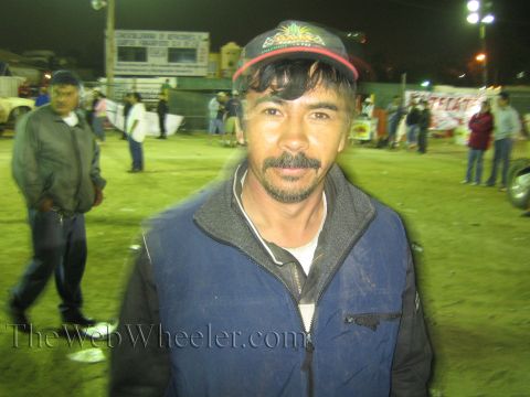 Man in a dark vest and cap with a mustache posing at a night dirt event