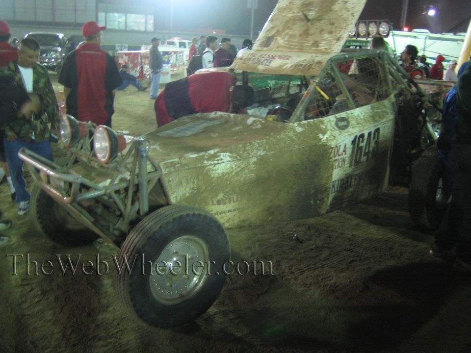 Front of a muddy tube-frame off-road buggy number 1643 in a dirt pit at night