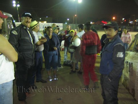 Group of people standing along a barrier at a night dirt racing event