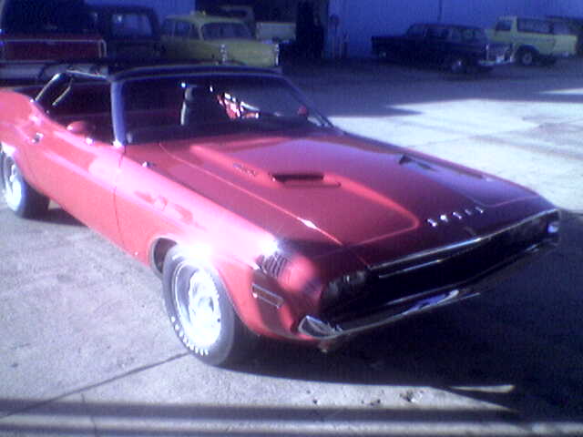 Red convertible muscle car, 3q front view. Other vehicles in background