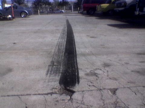 1988 Ford Bronco - Tire marks on asphalt with multiple vehicles parked in the background.